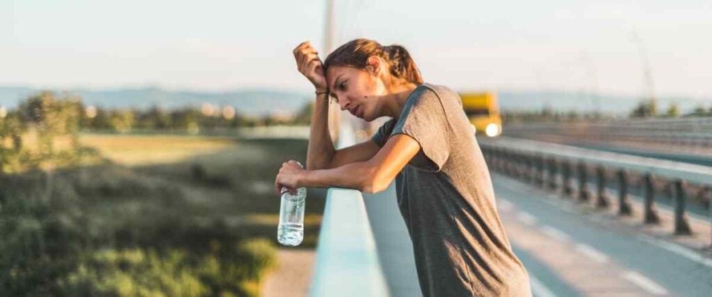 A woman after a run hunching over bridge with a bottle of water. 