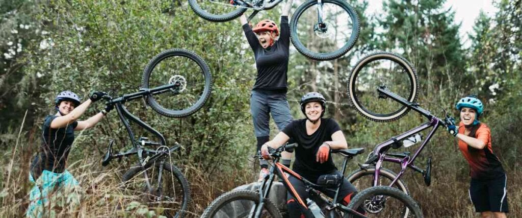 A group of women mountain bikers holding bikes with big smiles. 