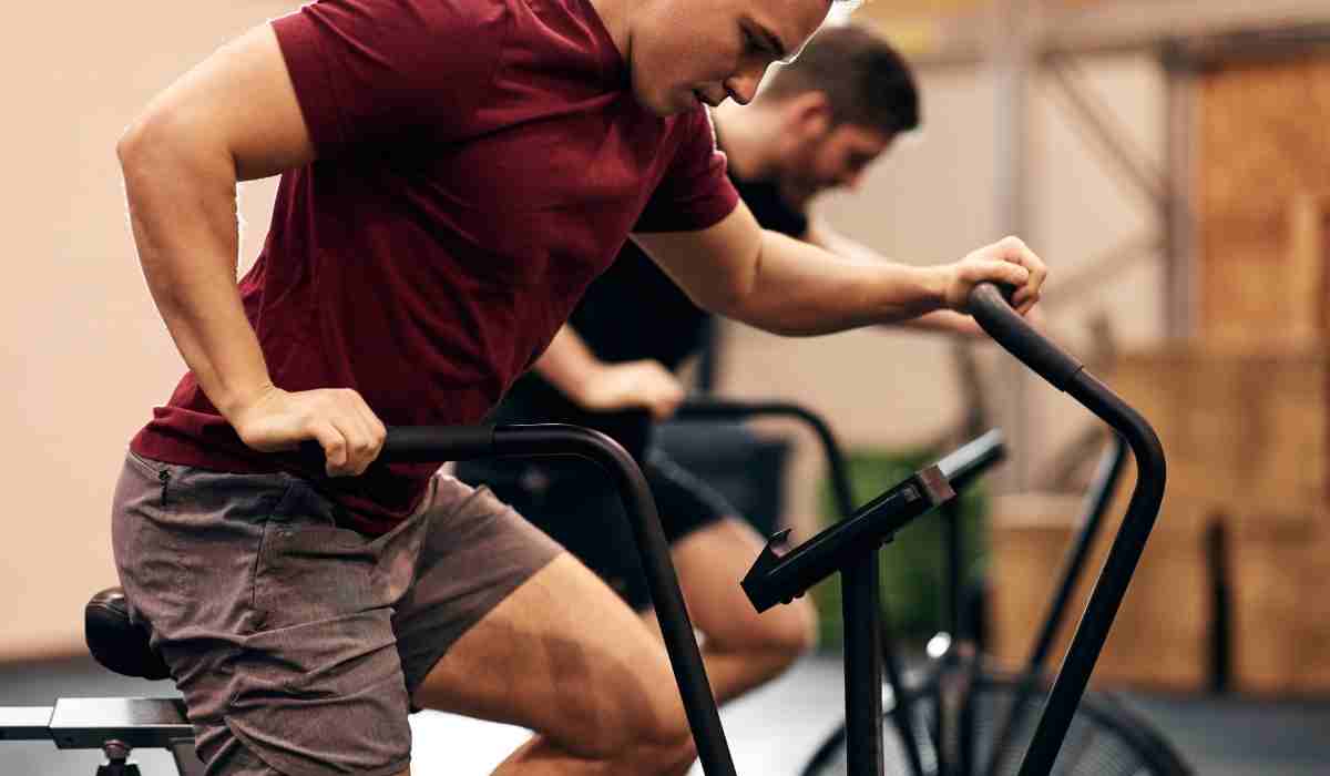Two men at the gym on indoor exercise bikes. 