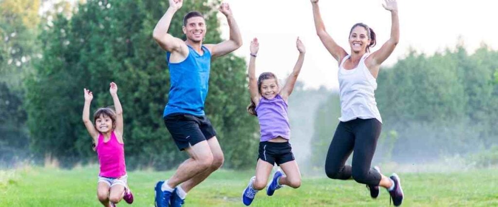 A family in workout clothes jumping and smiling at the camera. 