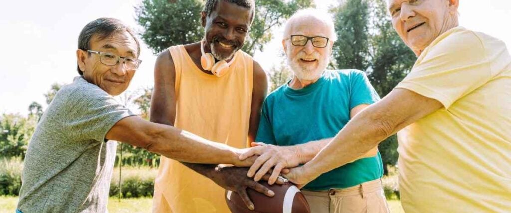 A group of older men holding a football smiling into the camera. 