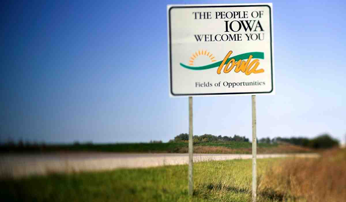 The welcome road sign in Iowa that reads "The People of Iowa Welcome You" on a empty road ahead. 