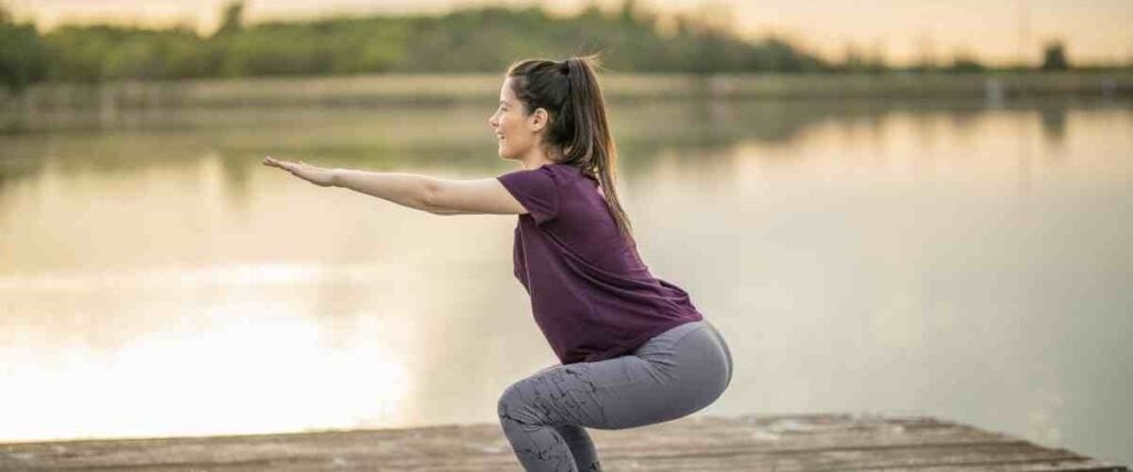 A woman doing a body weight squat on a lake pier. 