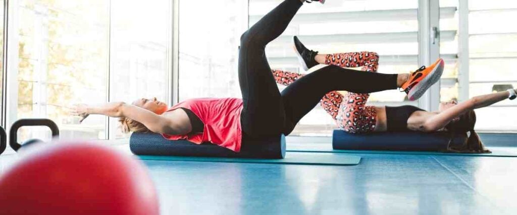 Two women doing the deadbug on yoga mats in the gym.
