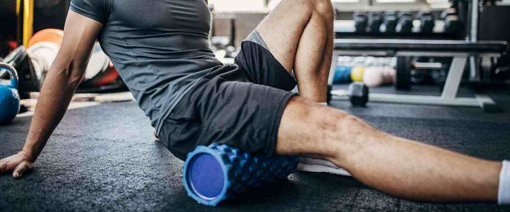 Man at gym foam rolling his glutes. 