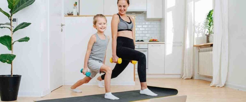 A man and her daughter doing forward lunges with weights in the kitchen. 