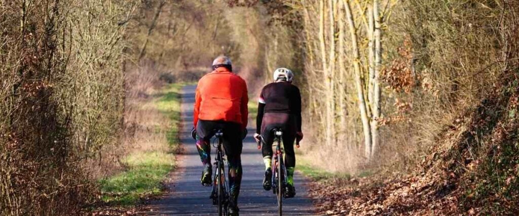 A couple biking down a shaded bike path in the fall.