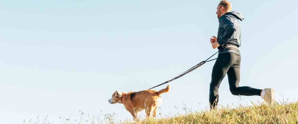 Man running with dog leash around waste looking ahead.