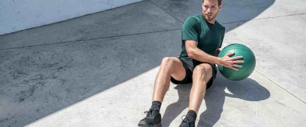 Man doing a Russian twist with a weighed ball on concrete.
