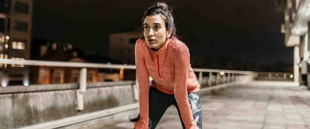 Female runner with her hands on her knees taking a breath outside while running at night. 