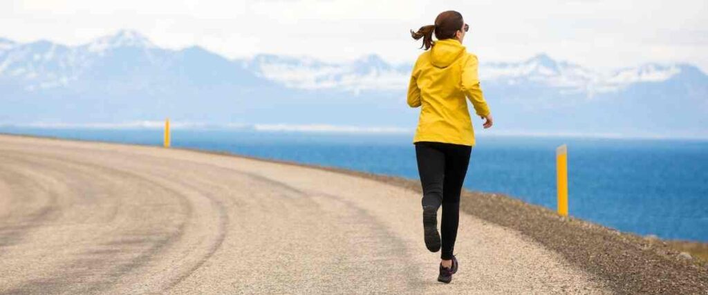 Woman running on road next to ocean and mountains.