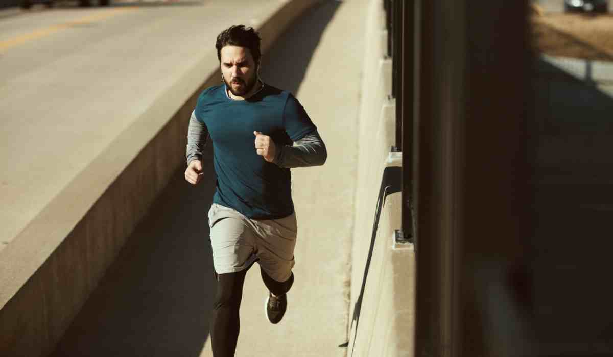 Man during a fast run on a running path next to a highway. 