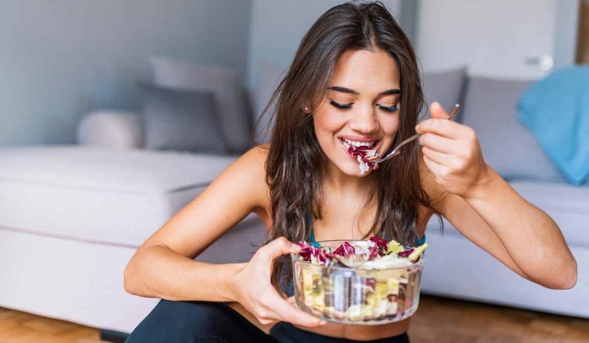 Woman eating a healthy salad next to her couch after a workout. 