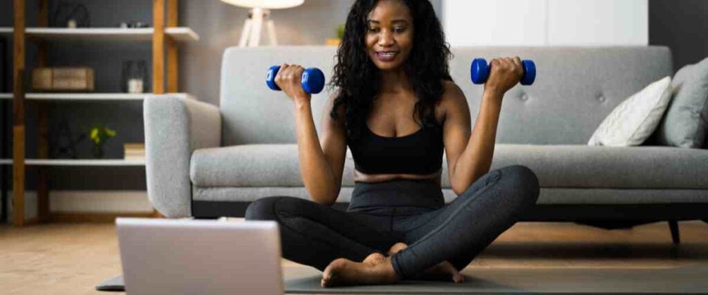 Woman hold weights on her yoga mat while watching her computer.