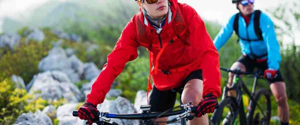 Two cyclists in mountain wearing gloves and waterproof coats.