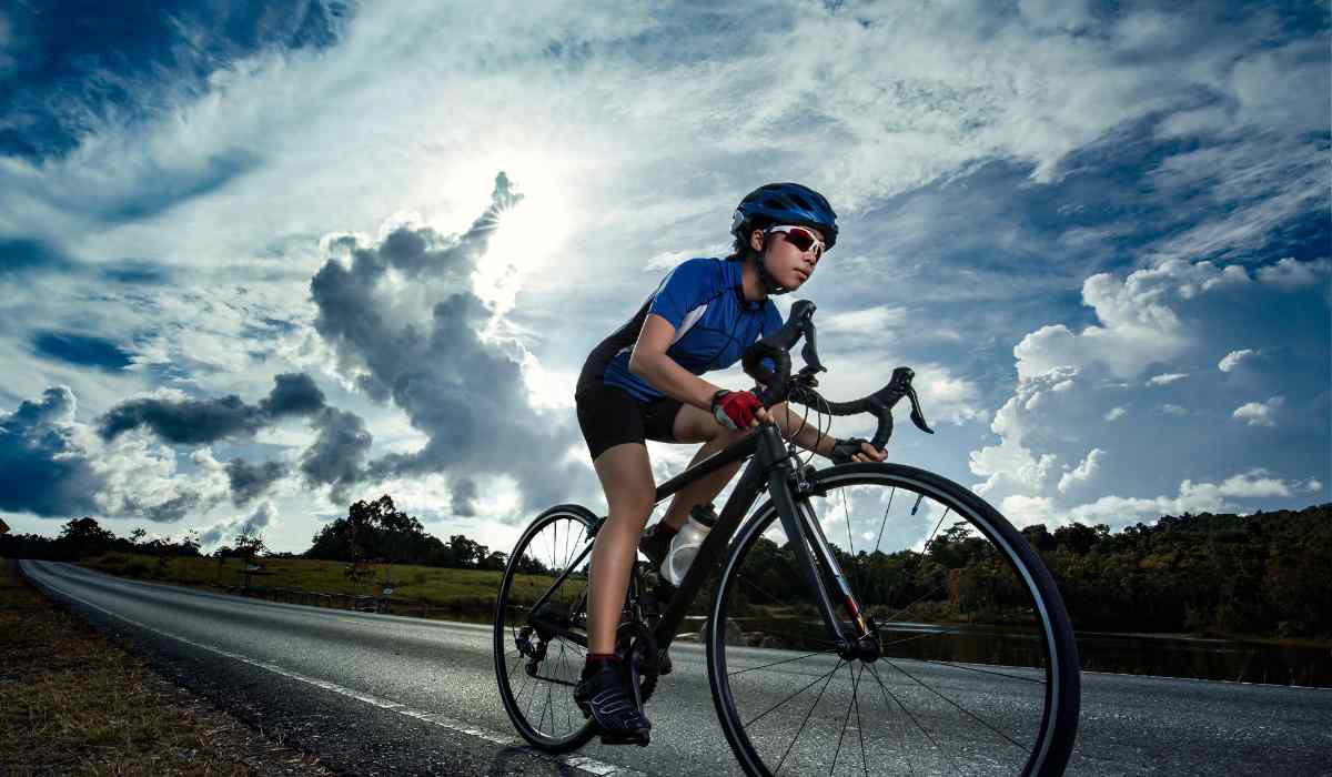 A female cyclists on a road with bright blue skies and clear shapes of the clouds. 