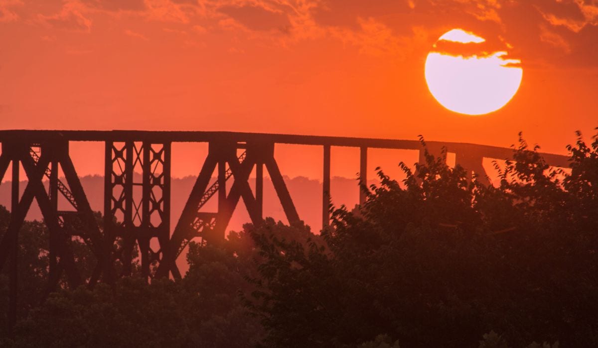 Orange sky with the view of a rail road bridge, forest and the sun. 