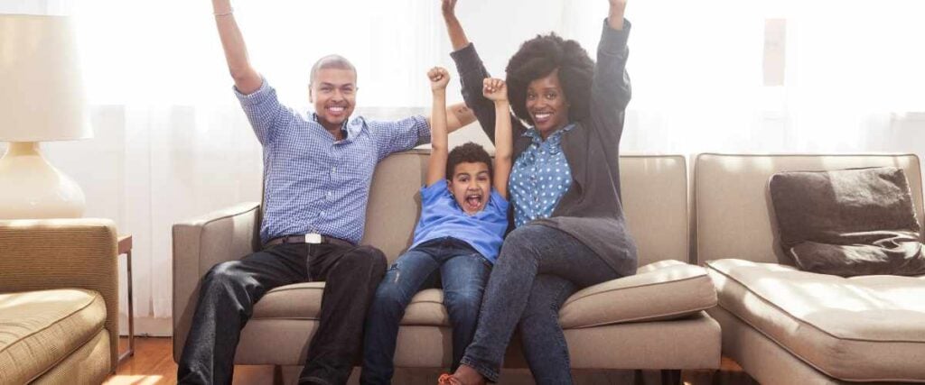 A family on a couch holding arms up with a big smile celebrating. 