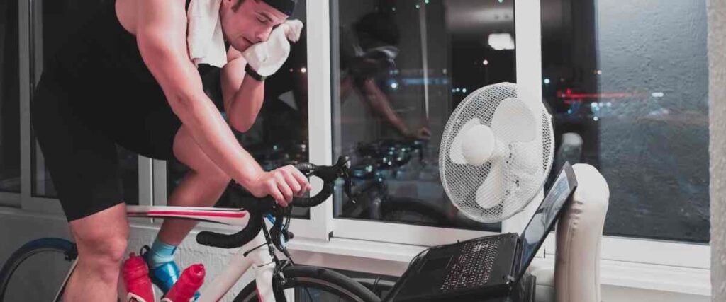 A male cyclists at home wiping his head with a towel from sweat. 