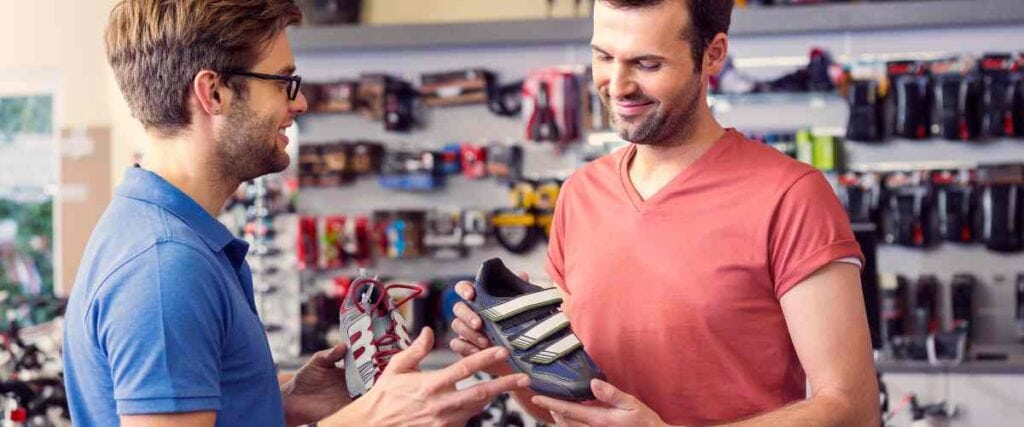 Two men at a bike shop looking at cycling shoes. 