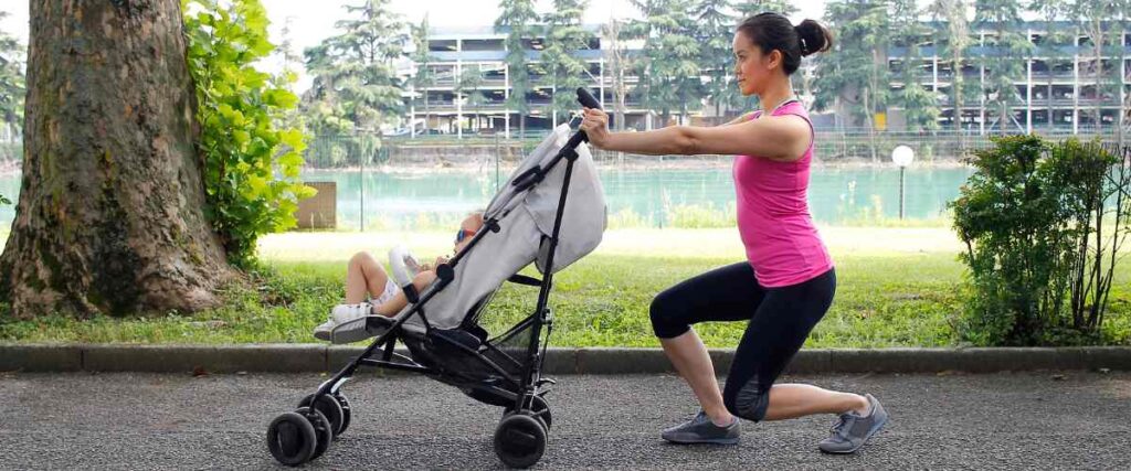 A mom doing a squat in the park while pushing a stroller with her kid in it. 
