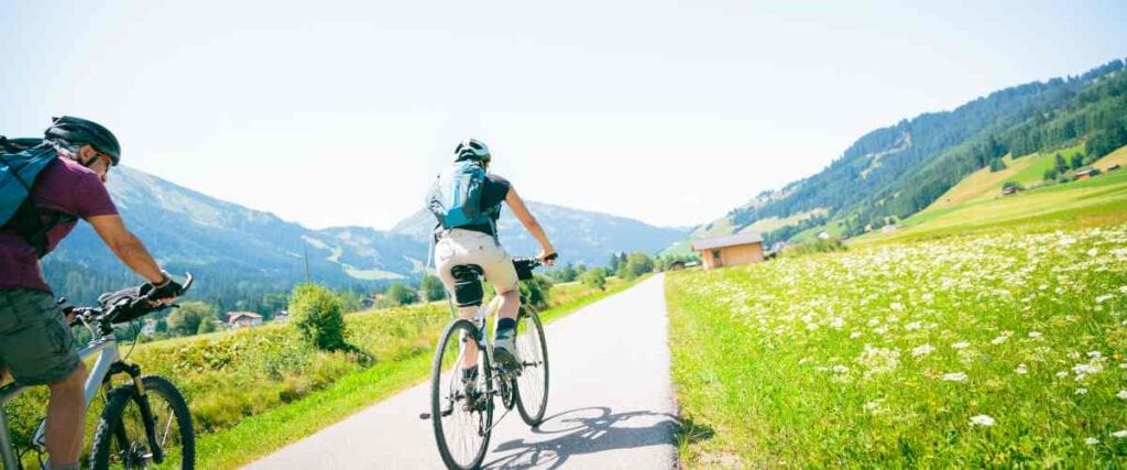 A couple on a bike path with loads of wild flowers. 