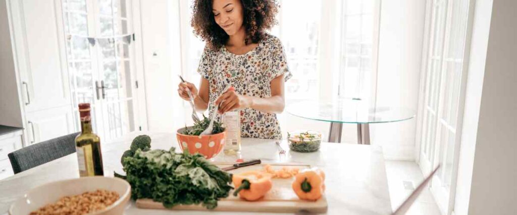 Woman in her kitchen preparing a big salad full of veggies. 