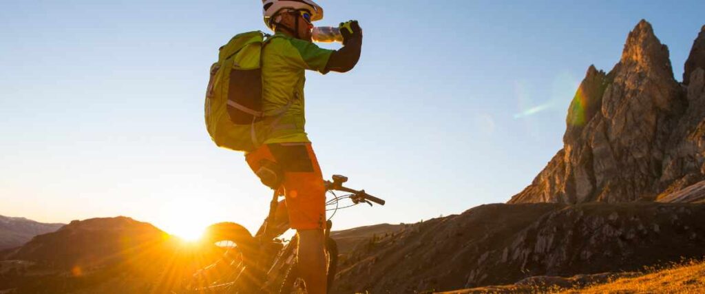 A mountain biker on a bike path taking a drink out of his water bottle. 