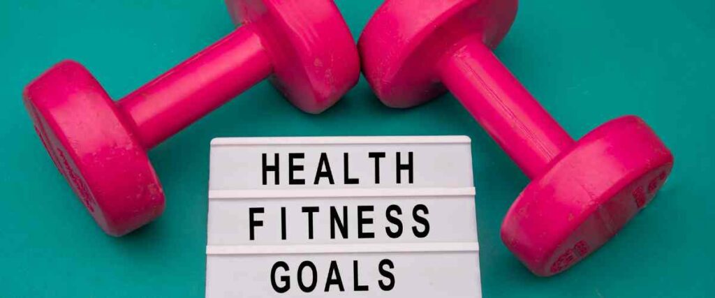 A sign with 'Health Fitness Goals' written on it, with two pink weights on top. 