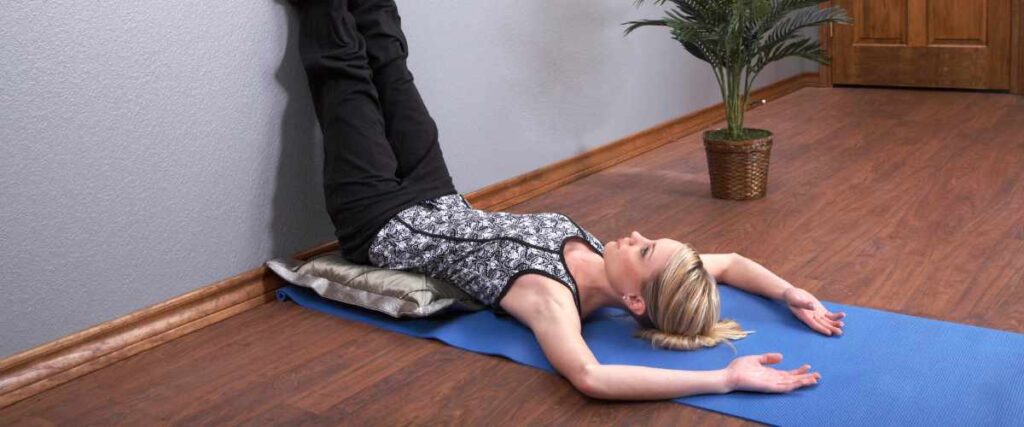 A woman on her yoga mat putting her legs against the wall with her arms over her head. 
