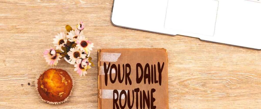A journal with the cover reading 'Your Daily Routine' next to a muffin and computer.