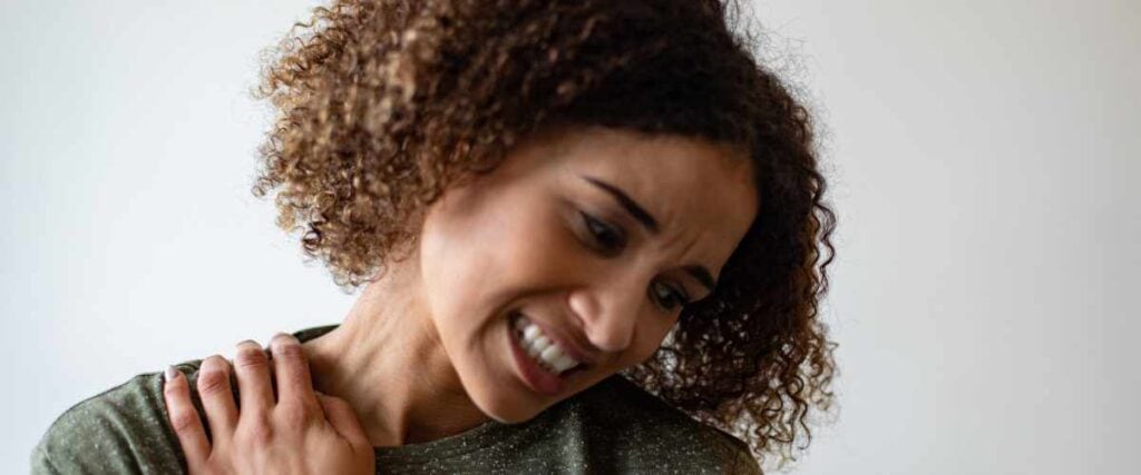 A woman massaging sore muscle on her shoulder. 