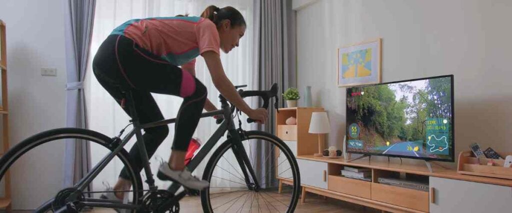 Female cyclists on her indoor trainer with wheels watching her tv screen during her fitness routine. 