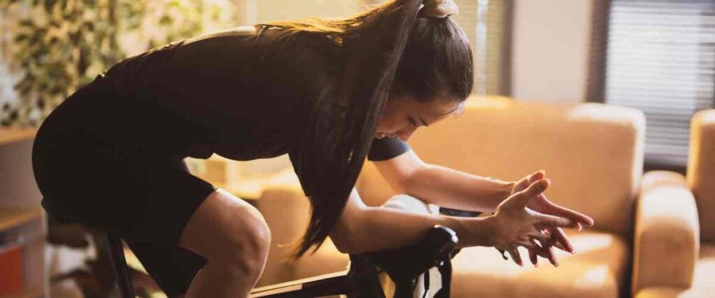 Female cyclists in her living room hanging her body her her bike after a long workout. 