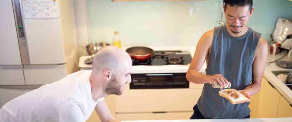 Two men in a kitchen making breakfast before their workout. 