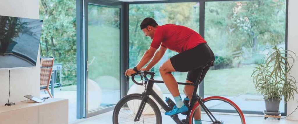 Male cyclists on his indoor bike trainer in his living room with all windows. 