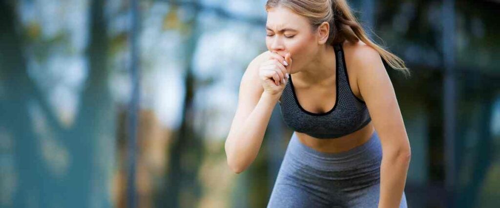 A woman hunched over coughing after her run outside. 