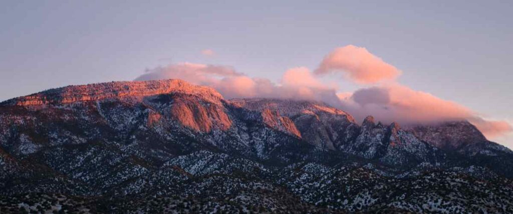 View of the Sandia Peak during sunset with clouds hover over the top of the peak. 