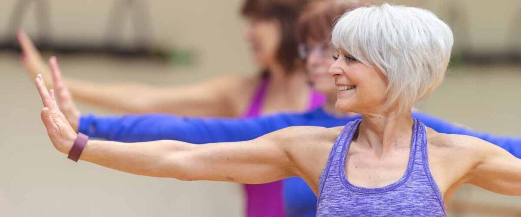Older women stretching in the gym with a big smile in their faces.