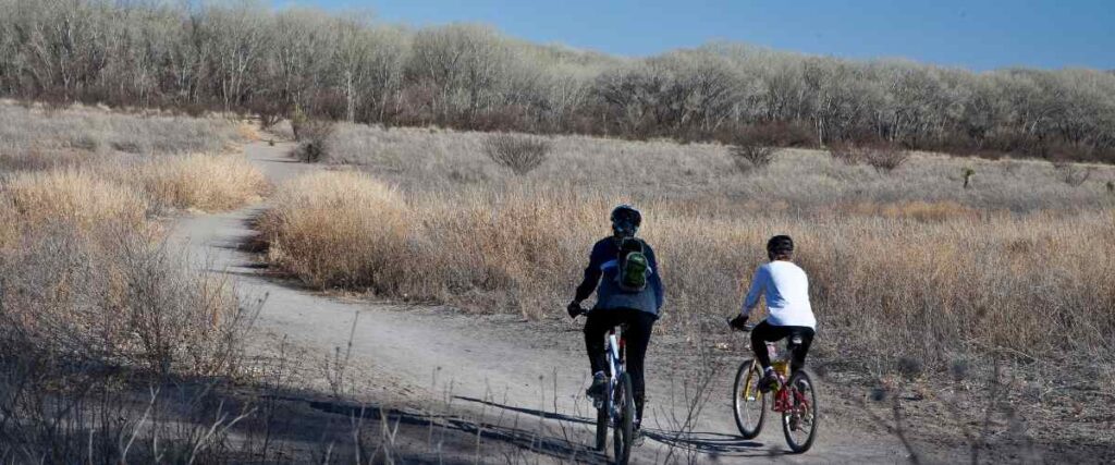 Two cyclists on a flat path on the Spring River Recreation Trail in New Mexico.