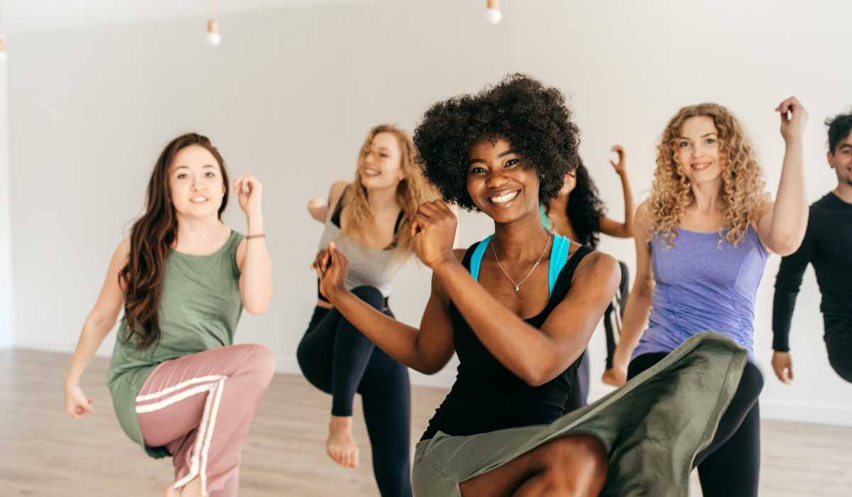 A group of women dancing at the gym with big smiles on their face. 