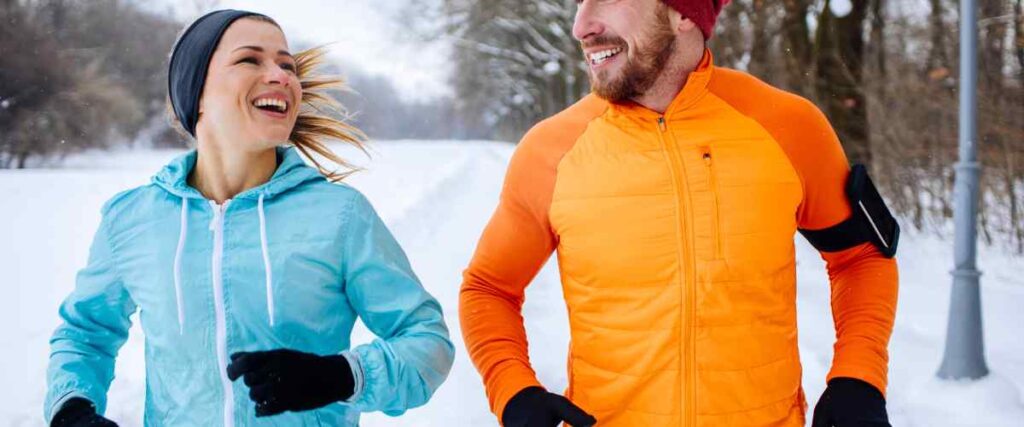 A couple running on a winter day smiling at each other during the day.