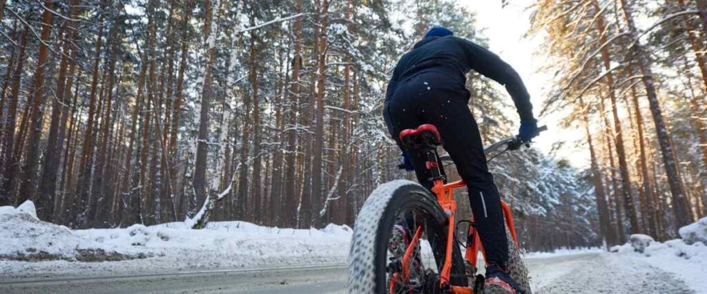 A man using his winter bike cycling in the snow on a road. 