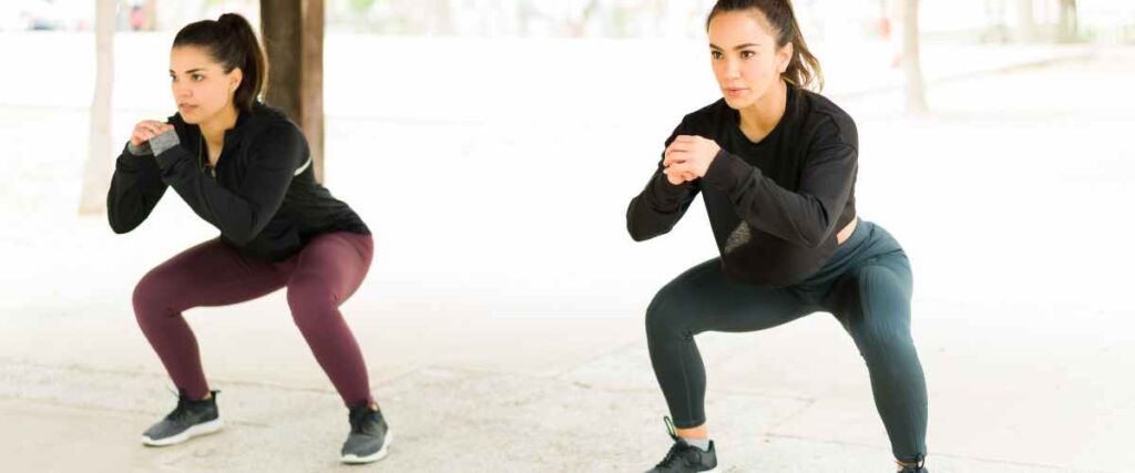 Two women doing lunges at a park looking forward. 