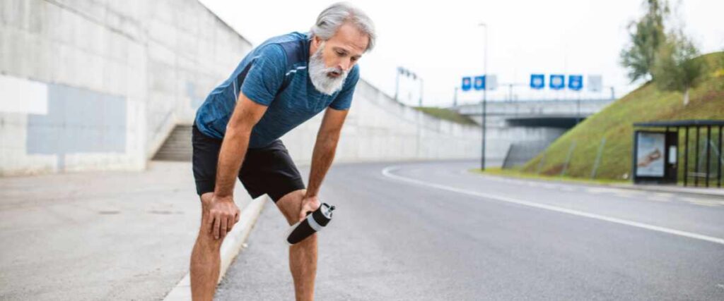A older runner bent over on the side of the road taking a breath. 
