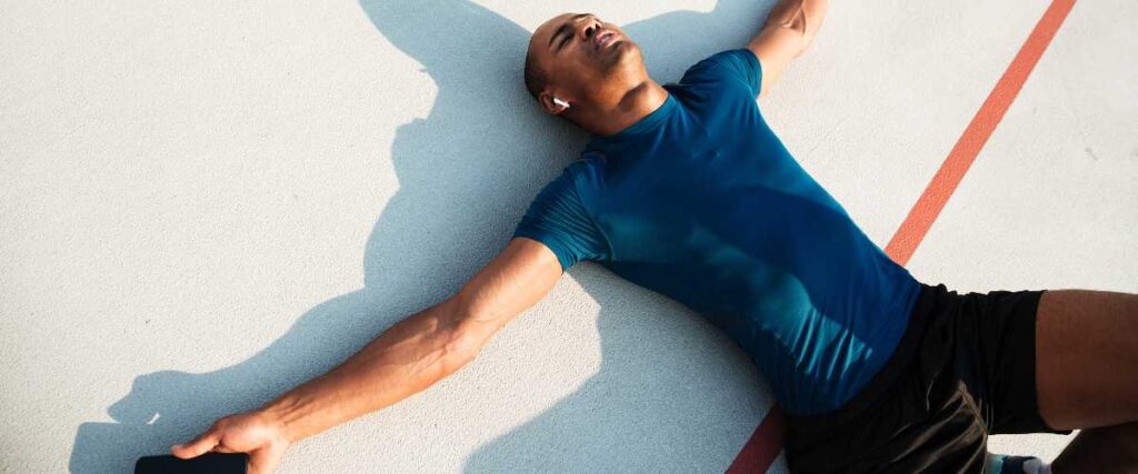 A man sprawled out on a track field tired after a hard training session.