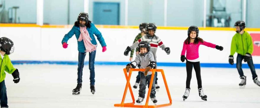 A group of kids ice skating together wearing helmets with big smiles. 