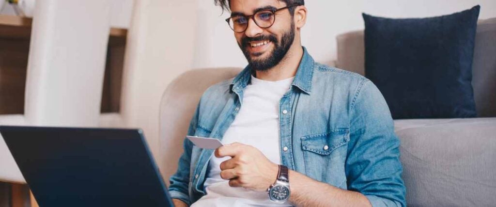 A man looking at his computer with his credit card out in his living room looking at bikes. 