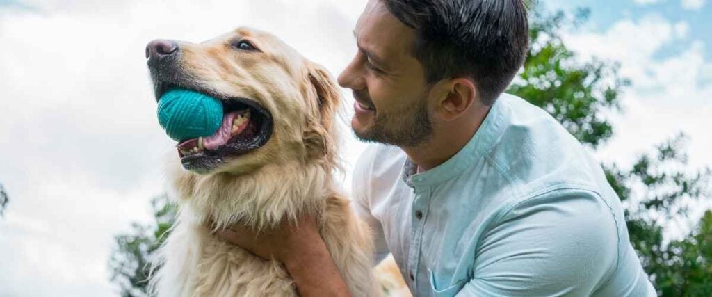 A man hugging his dog as they play fetch together.