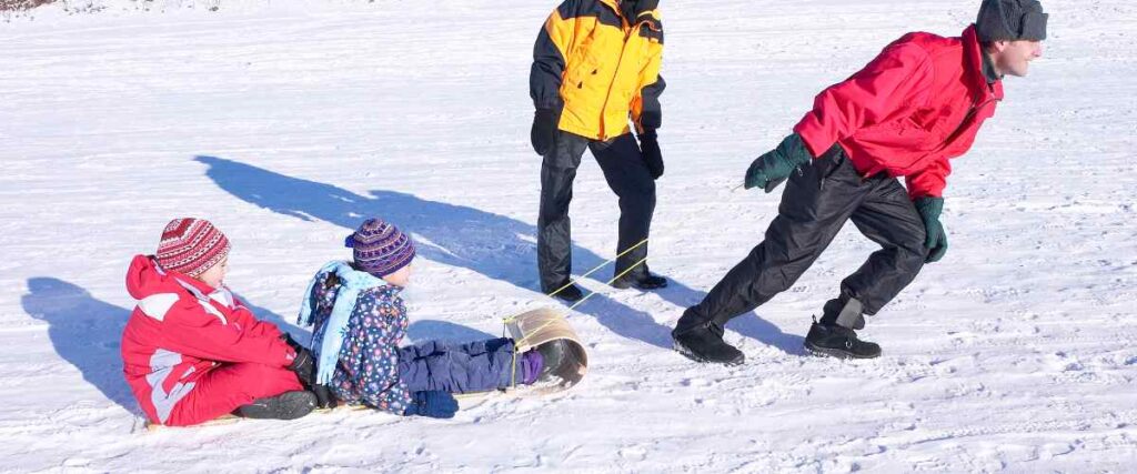 A family sledding together, and the dad pulling the kids on the sled before going up the hill. 